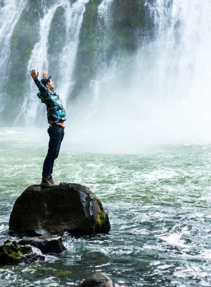 man standing on black rock surrounded body of water